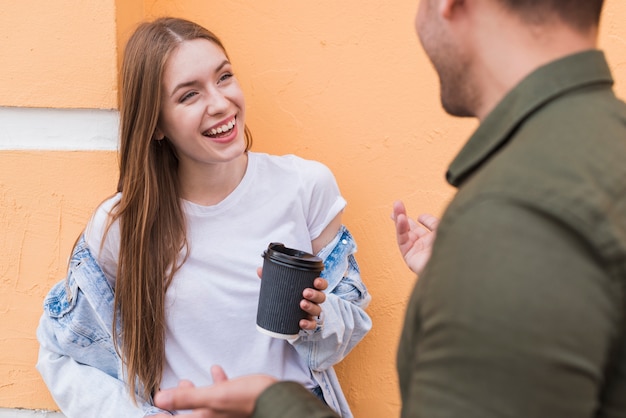 彼女のボーイフレンドと話しながら使い捨てのカップを保持している女性の笑顔