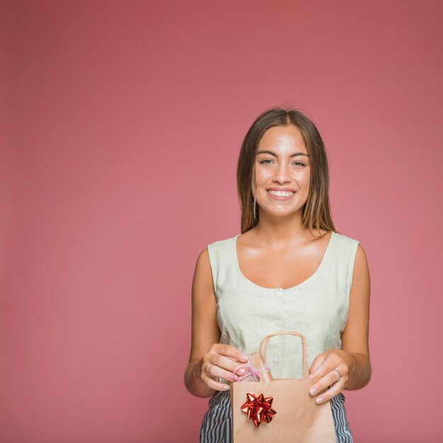 Smiling woman holding gift box from shopping bag against colored backdrop