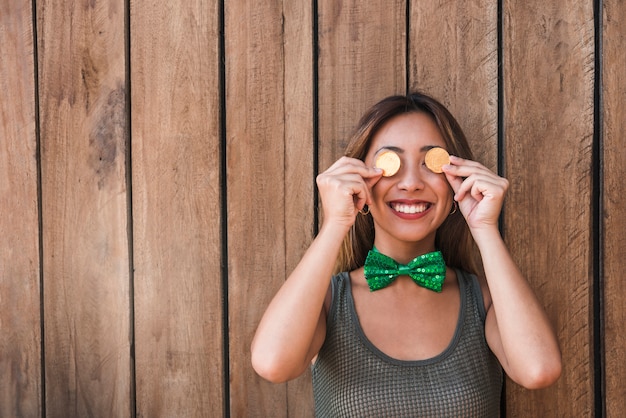 Free photo smiling woman holding golden coins near eyes