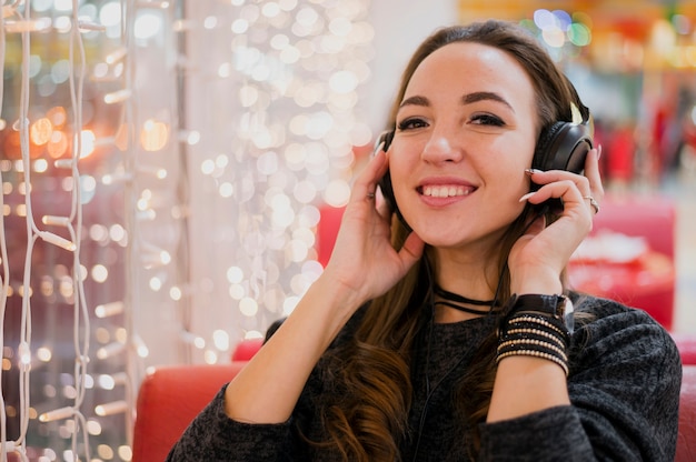クリスマスライトの近くの頭の上のヘッドフォンを保持している女性の笑みを浮かべてください。