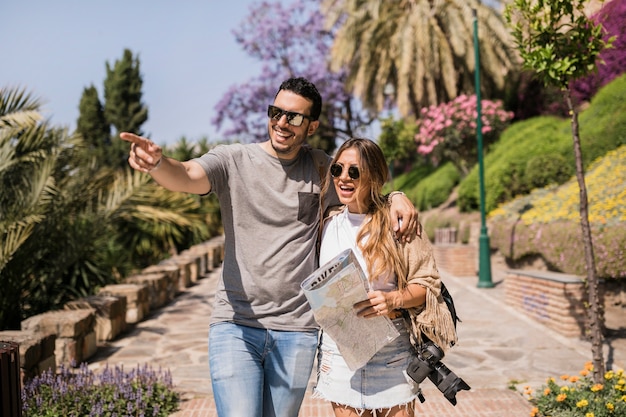 Smiling woman holding map looking at man pointing finger in the park