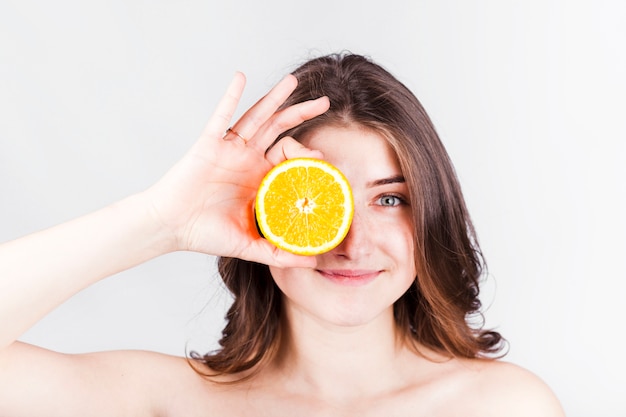 Smiling woman holding orange slice at face