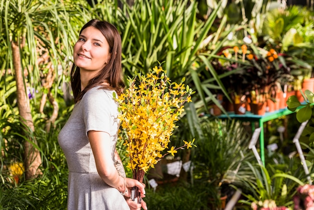 Smiling woman holding plant twigs from back