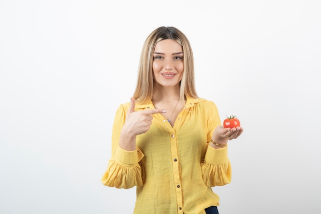 Smiling woman holding red tomato and posing on white.