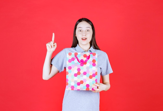 Smiling woman holding shopping bag and point finger up