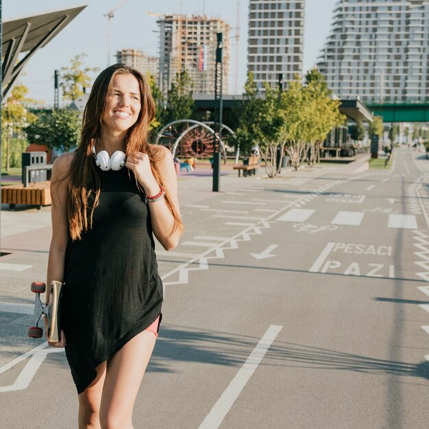 Smiling woman holding skateboard walking on street