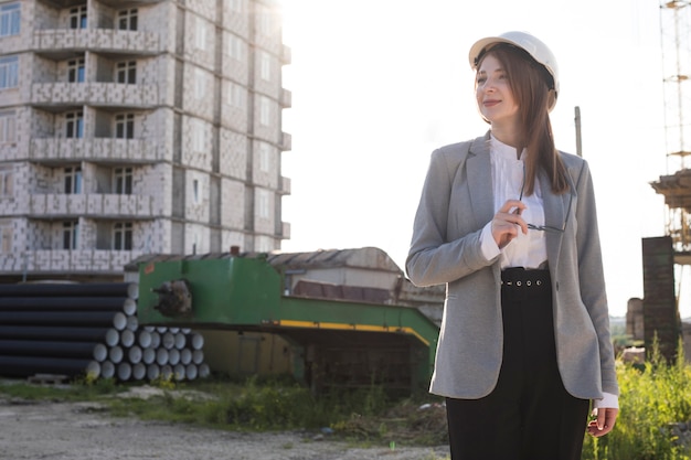 Free photo smiling woman holding spectacle standing at construction site looking away