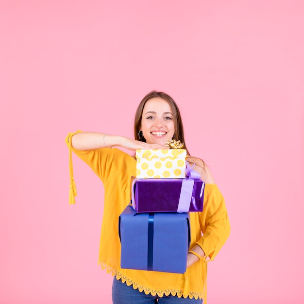 Smiling woman holding stack of gift boxes against pink background