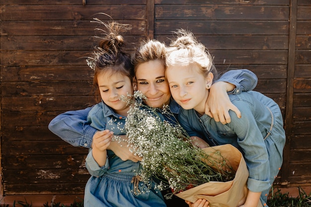 Smiling woman hugging daughters with bouquet