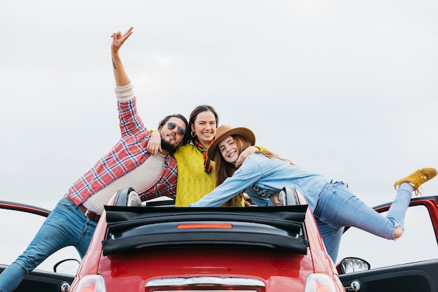 Smiling woman hugging happy man and cheerful lady and leaning out from car
