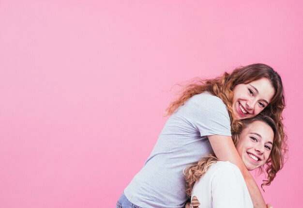 ピンクの背景に彼女の妹を抱擁する笑顔の女性