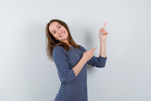 The smiling woman is pointing up with forefingers on white background