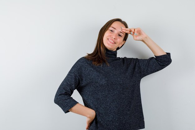 The smiling woman is putting forefinger on forehead and other hand on waist on white background