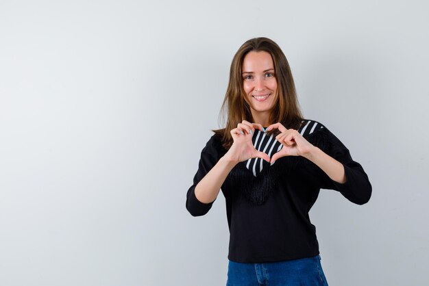 The smiling woman is showing heart gesture with hands on white background