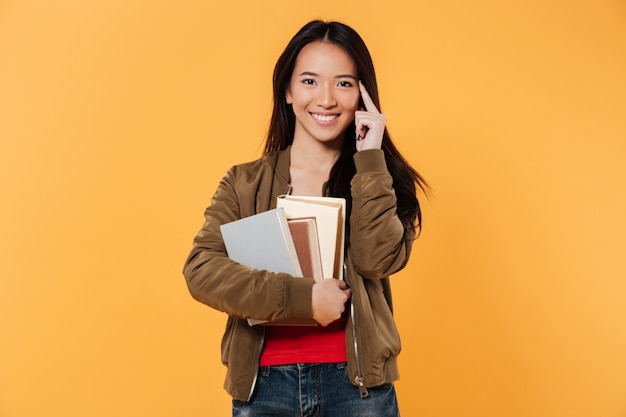 Smiling woman in jacket holding books while looking at camera