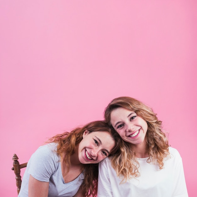 Smiling woman leaning head on her friend's shoulder against pink backdrop