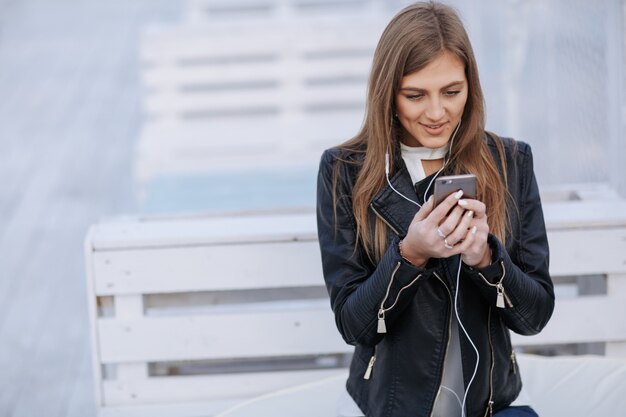 Smiling woman listening to music with white headset looking at her phone