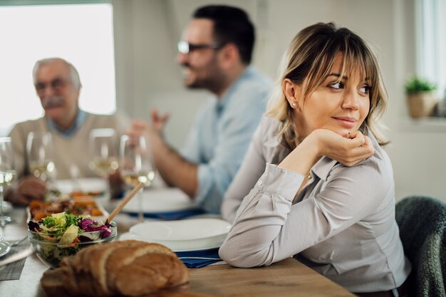 Foto gratuita donna sorridente che distoglie lo sguardo mentre si siede al tavolo da pranzo con la sua famiglia