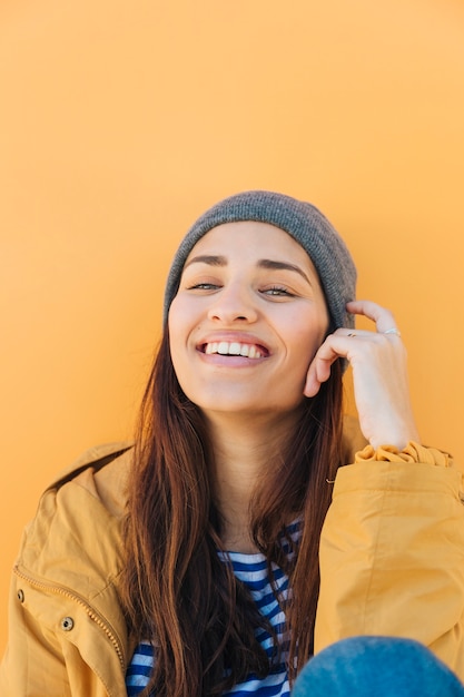 Foto gratuita donna sorridente che guarda l'obbiettivo seduto di fronte a superficie gialla