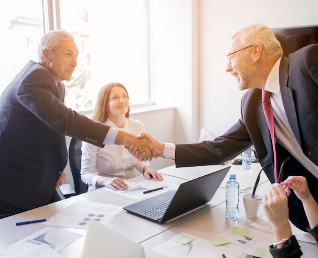 Smiling woman looking at two senior businessman shaking hands