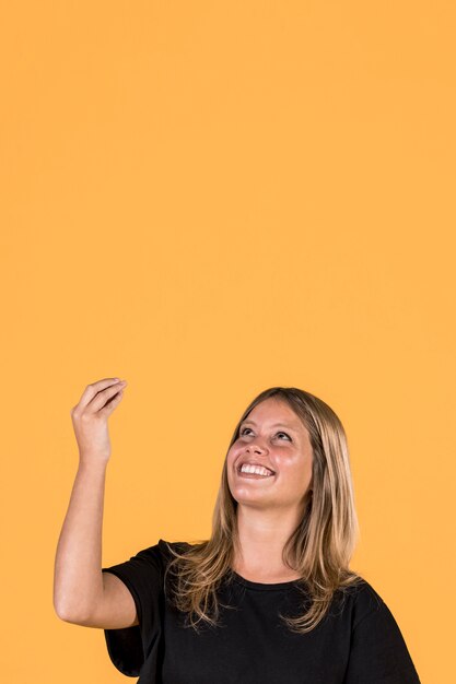 Smiling woman looking up and gesturing on yellow wall background