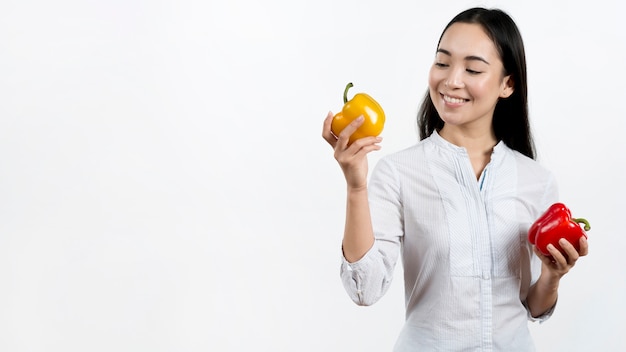 Free photo smiling woman looking at yellow bell pepper standing against white backdrop