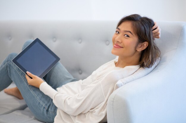 Smiling woman lying on coach with pc tablet and touching hair