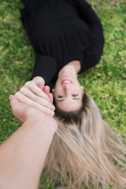 A smiling woman lying on lawn holding man's hand