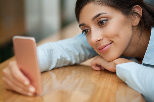 Smiling Woman Lying on Table with Smartphone