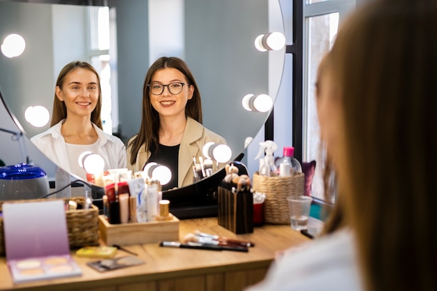 Smiling woman and makeup artist looking at mirror