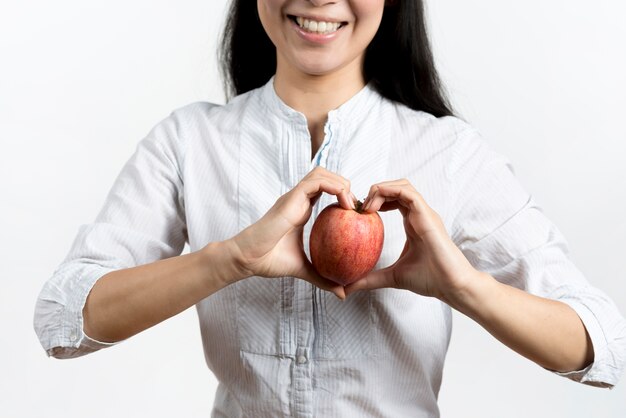 Smiling woman making heart shape with apple over white backdrop