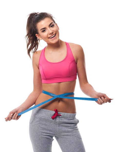 Smiling woman measuring her waist line with tape measure