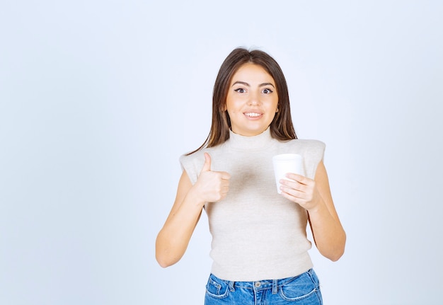 A smiling woman model holding a plastic cup and showing a thumb up.