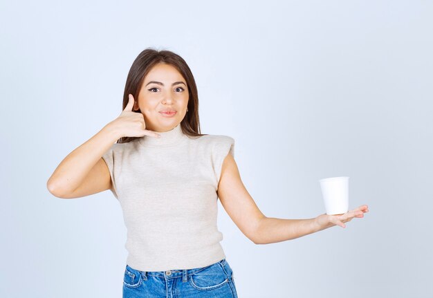 プラスチック製のコップを見せて、電話のジェスチャーで話している笑顔の女性モデル。