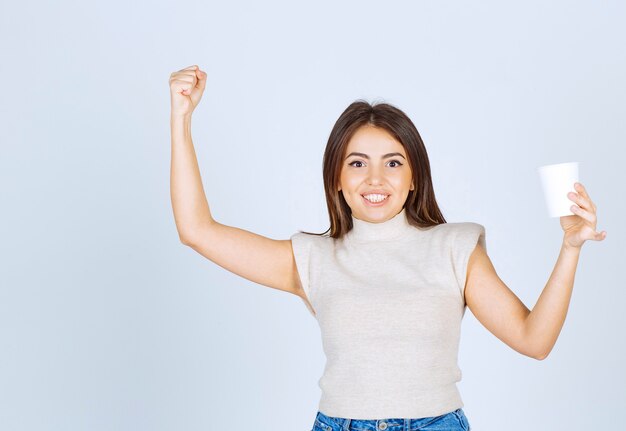 プラスチック製のコップを見せてポーズをとる笑顔の女性モデル。