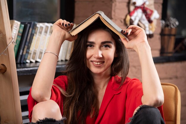 Smiling woman model sitting and holding a book overhead.