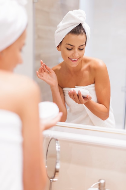 Smiling woman moisturizes skin after the shower