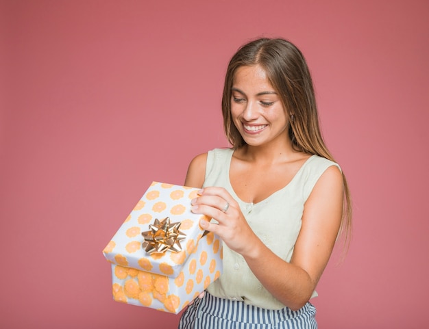 Foto gratuita donna sorridente che apre il contenitore di regalo floreale con l'arco dorato contro il contesto colorato