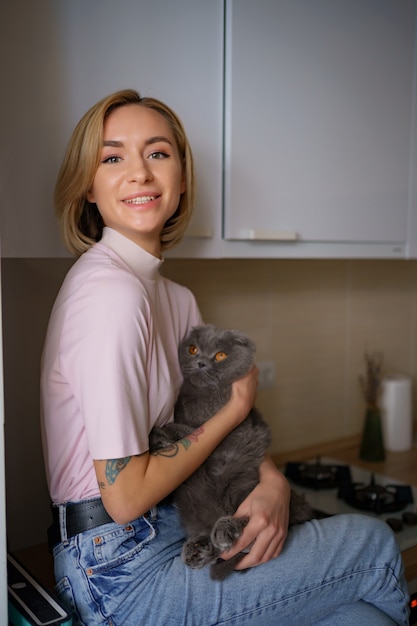 自宅のキッチンで猫と遊ぶ笑顔の女性。