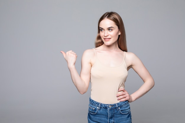 Smiling woman pointing away and looking at the camera over gray wall