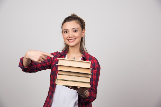 Foto gratuita una donna sorridente che indica una pila di libri.