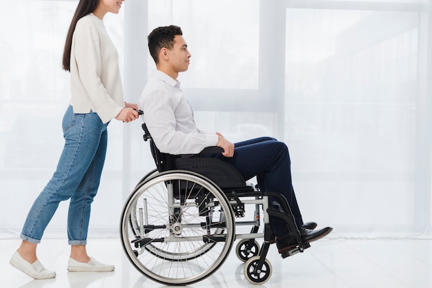 Улыбается женщина толкает молодого человека, сидящего в инвалидной коляске