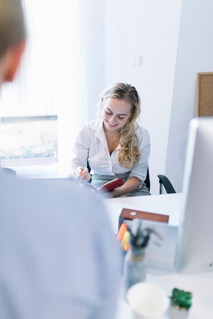 Free photo smiling woman reading diary in office during meeting