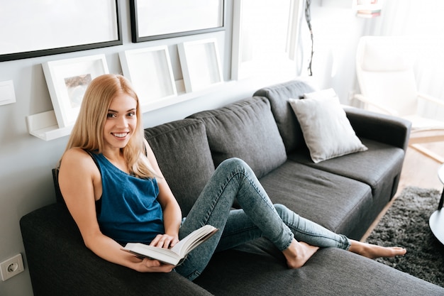 Smiling woman relaxing and reading book on sofa at home