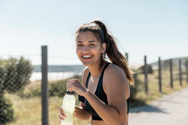 Foto gratuita donna sorridente che funziona e che tiene bottiglia con acqua