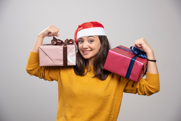 Smiling woman in Santa hat showing gift boxes. 