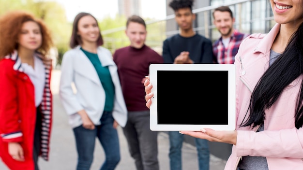 多重の人々の前で空白のデジタルタブレットを見せて笑顔の女性