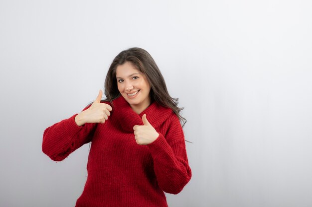 Smiling woman showing thumbs up over white wall.