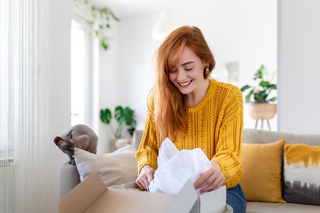 笑顔の女性が自宅のソファに座るオープンポストパッケージショッピングオンラインインターネットで商品を購入する幸せな若い女性の顧客が注文または配達に満足した郵便配送小包を開梱する