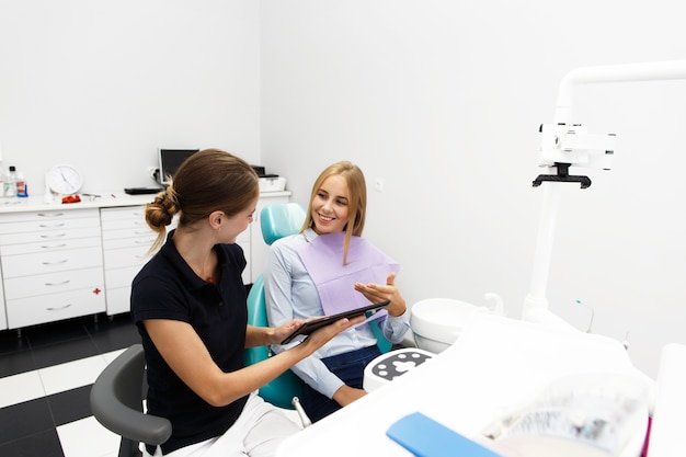 의사가 그녀의 뭔가를 보여주는 동안 웃는 여자 치과 의사의 사무실에서 의자에 앉아